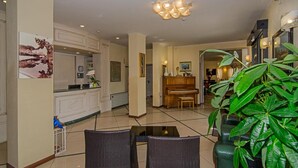 A spacious living area with a dining table, chairs, a piano, and a large green plant. - Hotel Villa Ombrosa (Pietrasanta)