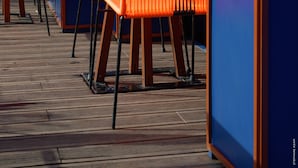 Outdoor seating with orange chairs and tables, a wooden deck, and a blue wall with a door. - 1K Paris (Paris)
