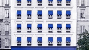 A multi-story hotel with a white facade and blue awnings. It has a ground-level restaurant-bar and a sign indicating a hotel on the right side. - 1K Paris (Paris)