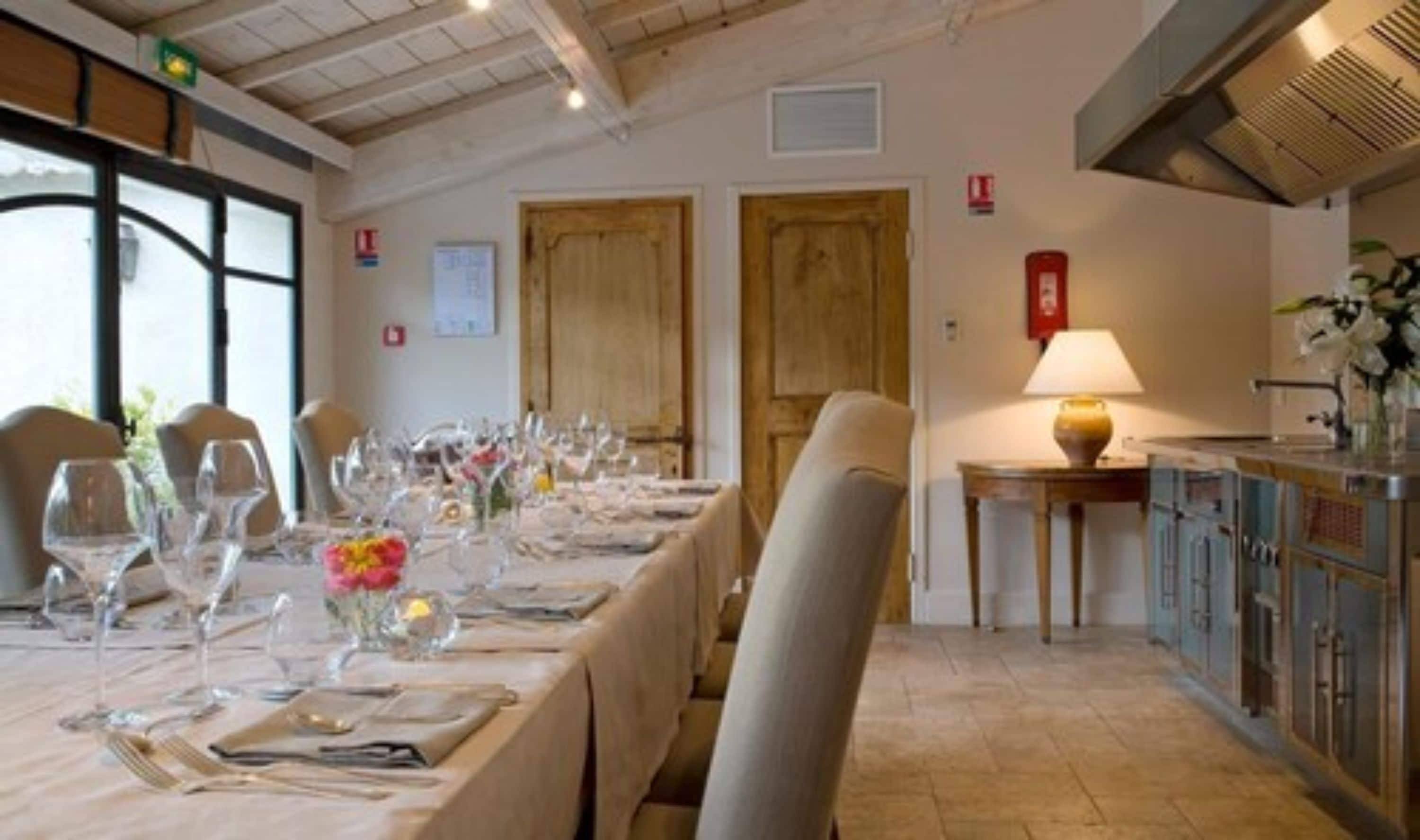 A dining area with a long table set for a meal, wooden doors, a fire alarm, and a kitchen area with cabinets.