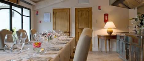 A dining area with a long table set for a meal, wooden doors, a fire alarm, and a kitchen area with cabinets.