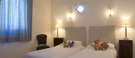 A room with two beds, a chair, a small table, and a decorative rug.