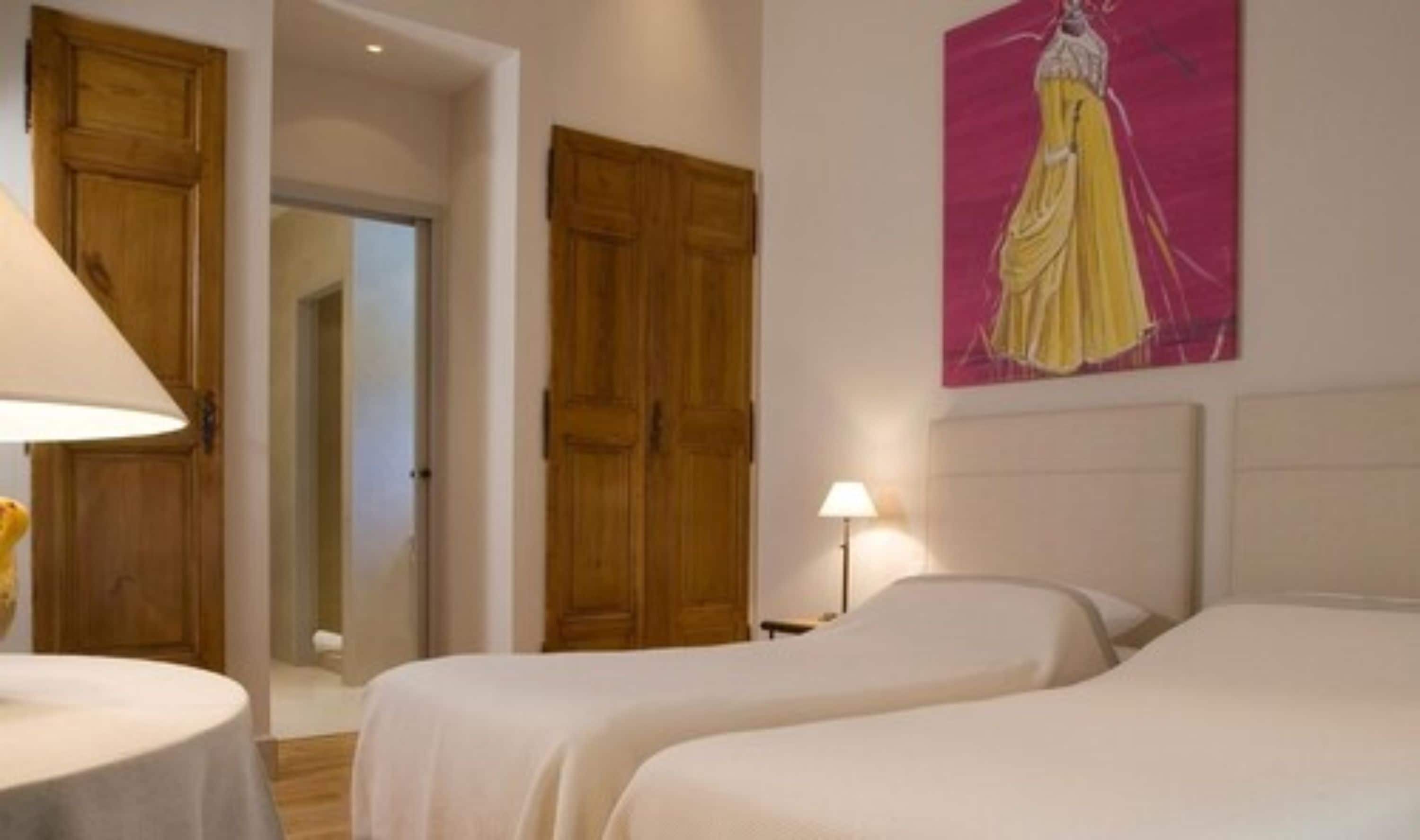 Une chambre d’hôtel avec deux lits, des armoires en bois, un tableau au mur et une lampe sur la table de chevet.