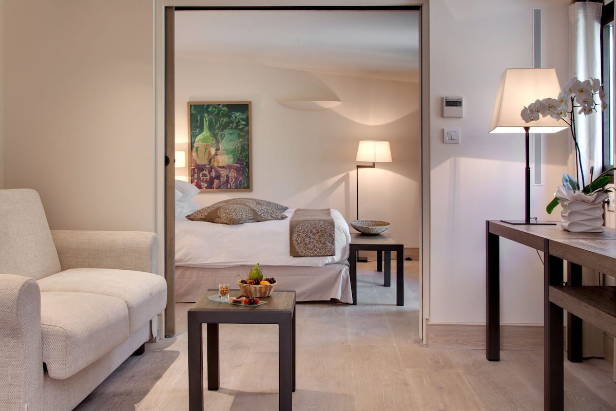 Une chambre d’hôtel moderne avec un canapé, une table à manger, un lit donnant sur un beau paysage et un tableau au mur.