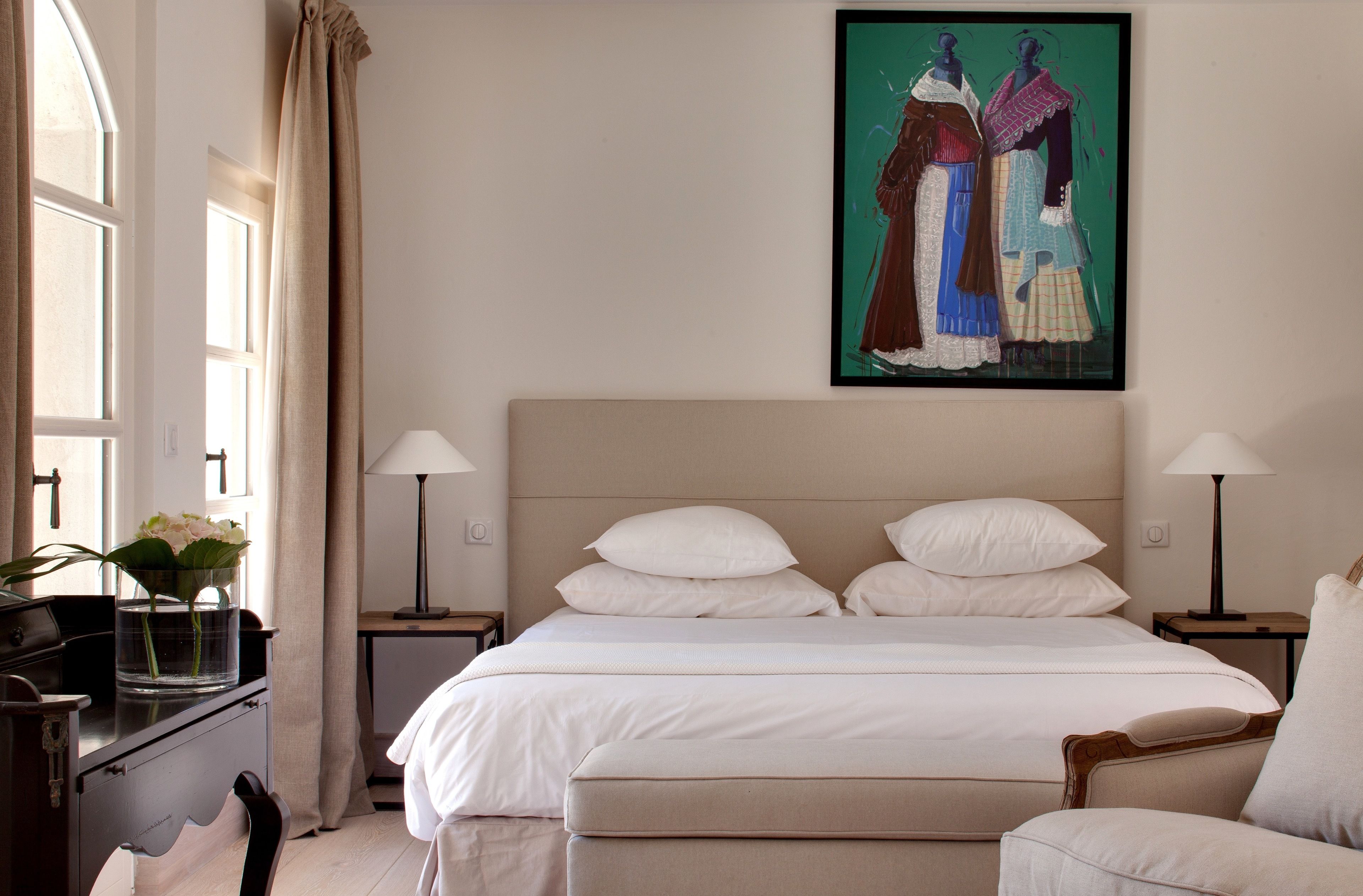 Une chambre à coucher bien rangée, avec un lit, deux tables de chevet, une chaise et un tableau accroché au mur.