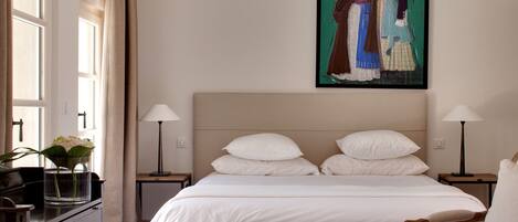Une chambre à coucher bien rangée, avec un lit, deux tables de chevet, une chaise et un tableau accroché au mur.