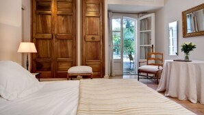 Un dormitorio con una cama grande, un armario de madera, una mesita con una silla y una ventana con vistas al verdor.