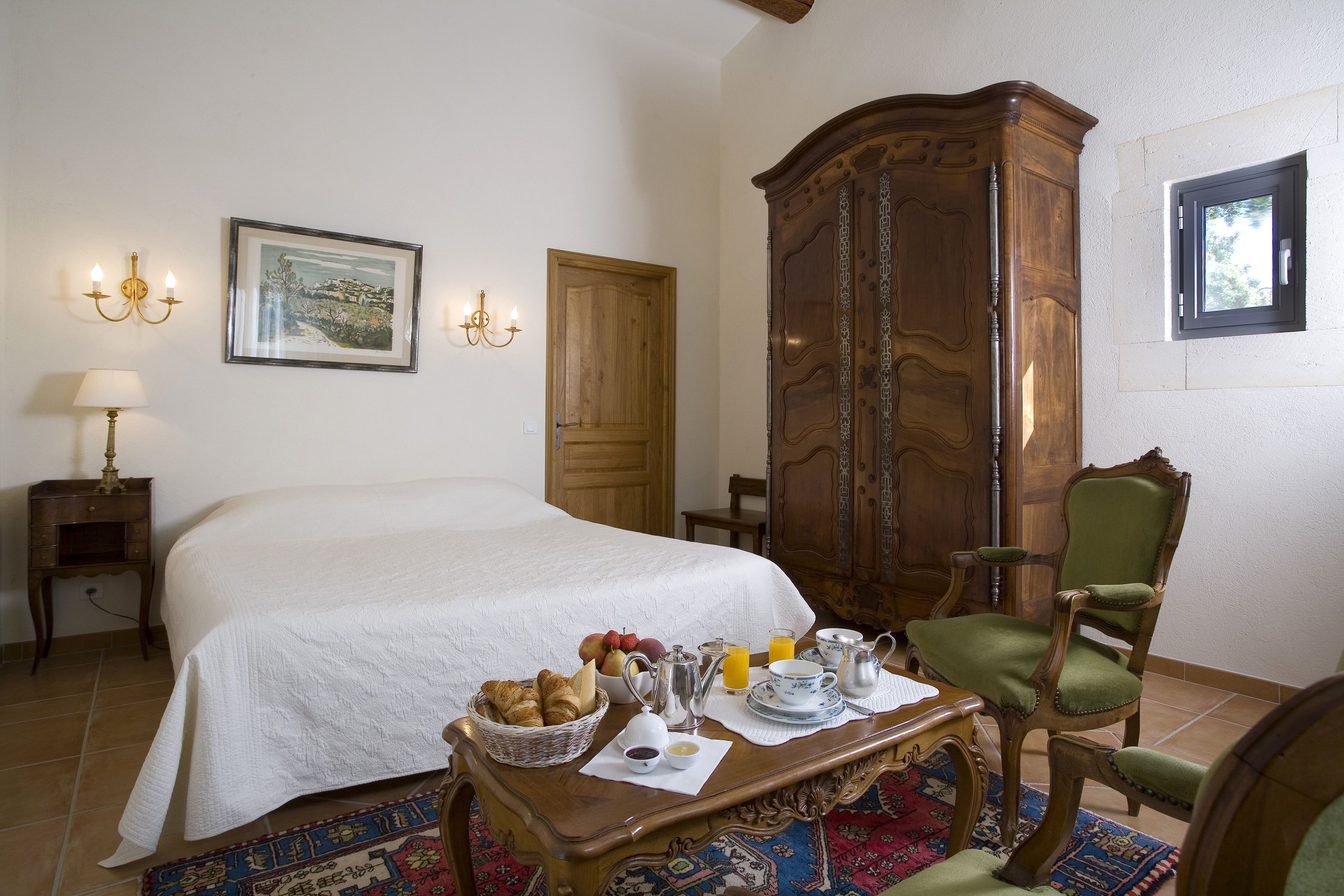 Un dormitorio ordenado con cama, bandeja de desayuno, armario de madera y un sillón verde.