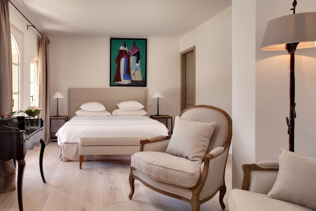 Une chambre à coucher avec un lit, deux tables de chevet avec des lampes, une chaise, un bureau et un tableau au mur.