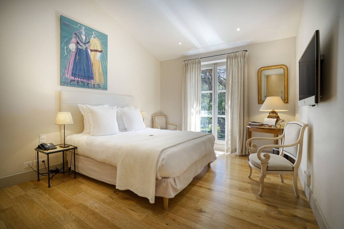 Une chambre d’hôtel avec un grand lit, des lampes de chevet, un bureau avec une chaise, une télévision et une fenêtre avec des rideaux.