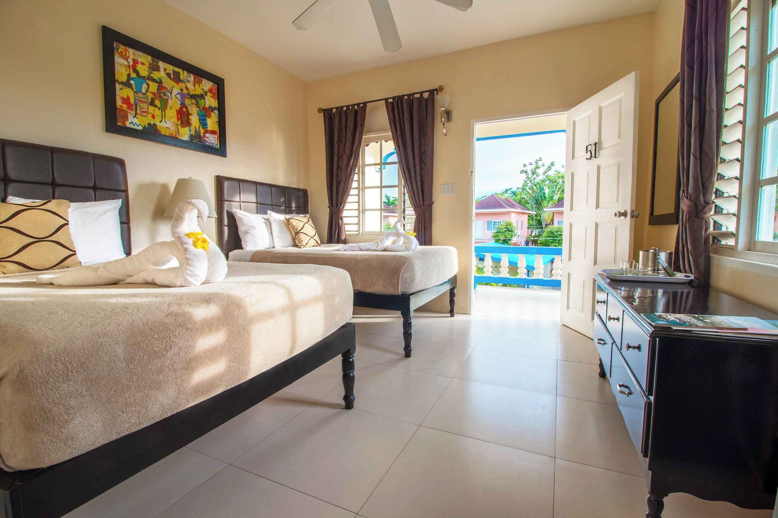 Habitación de hotel con dos camas, un aparador, un ventilador de techo y vistas al exterior.