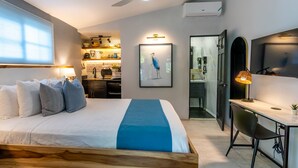 Un dormitorio con cama, mesita de noche, lámpara y vistas a la cocina y el baño.