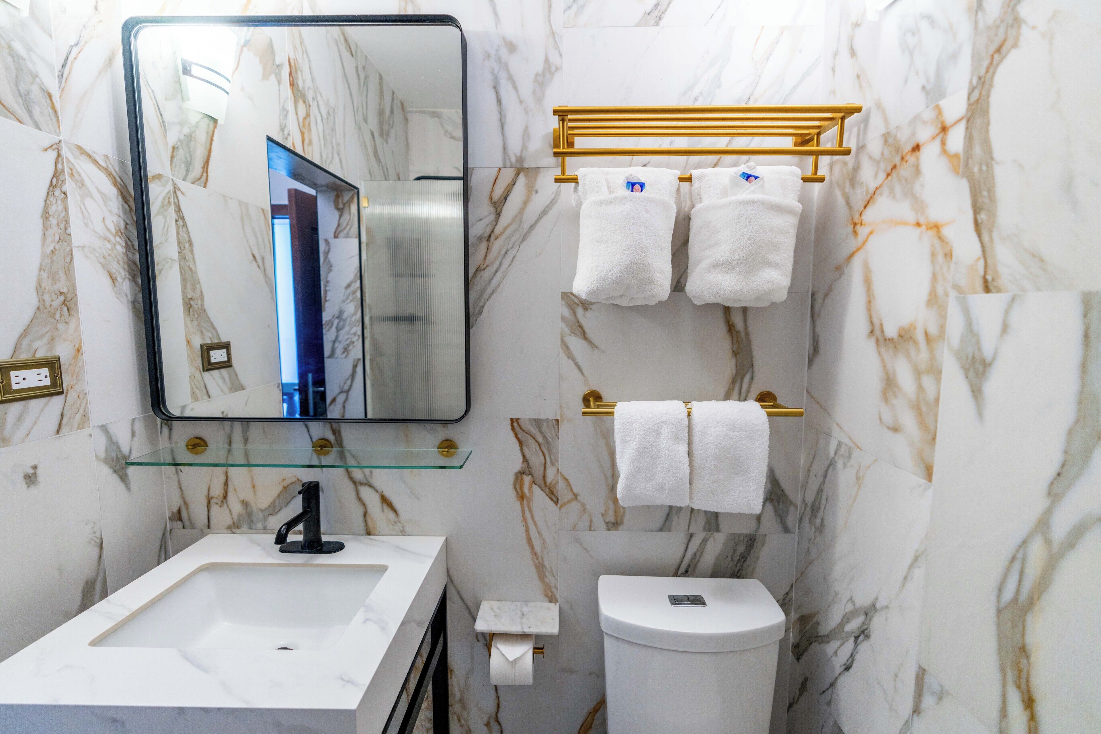 A bathroom with a marble wall, a sink, a toilet, and a towel rack.