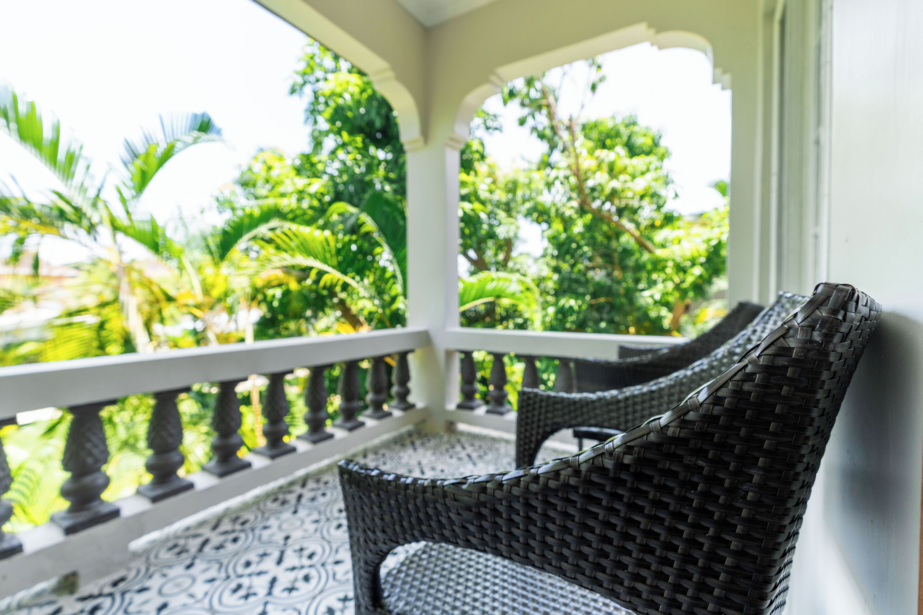 Un espacio de estar al aire libre cubierto con mobiliario de mimbre, piso estampado y vistas a exuberante follaje.
