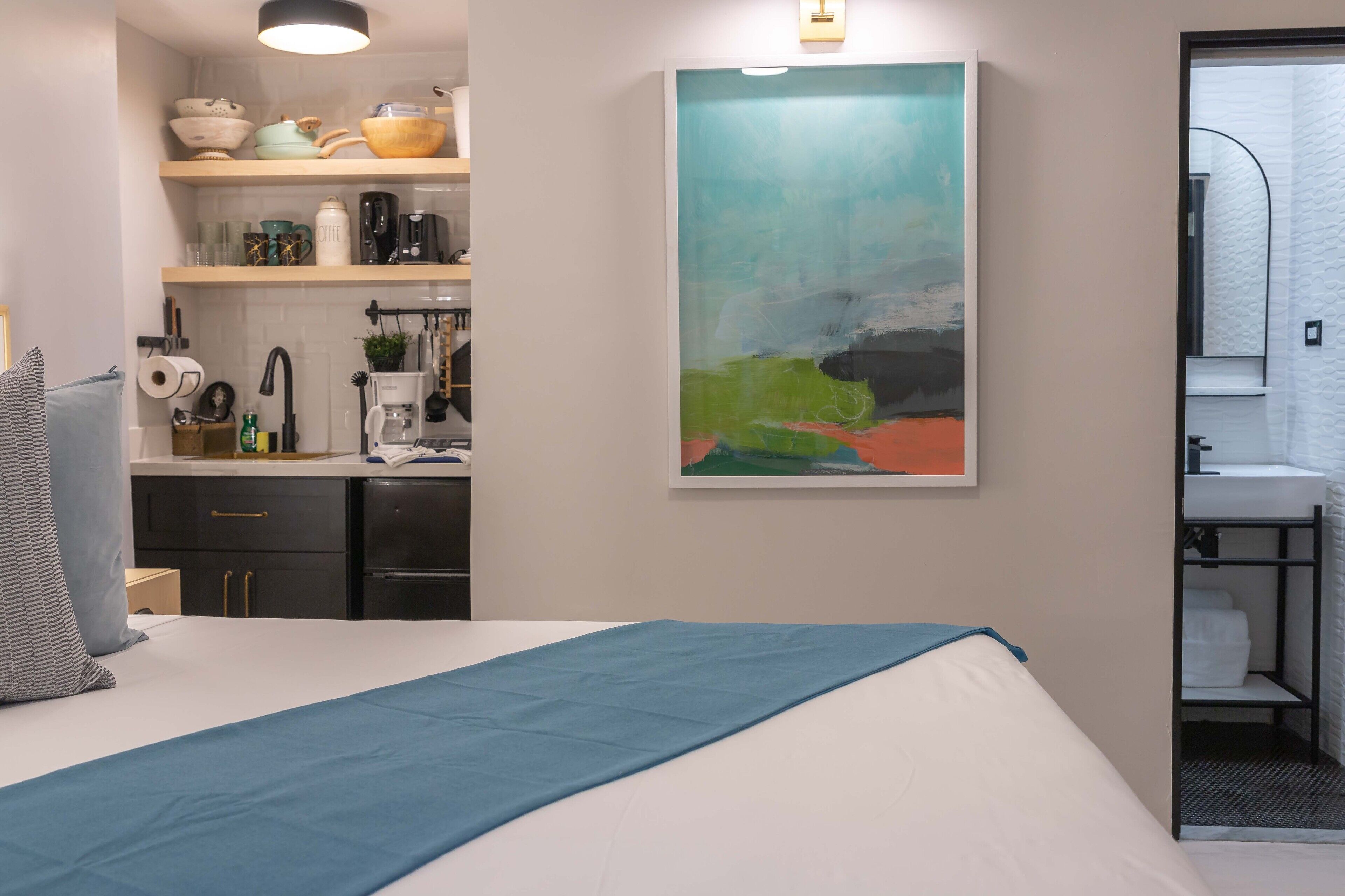 Una camera d'albergo con un letto, un quadro, un angolo cottura e un bagno.