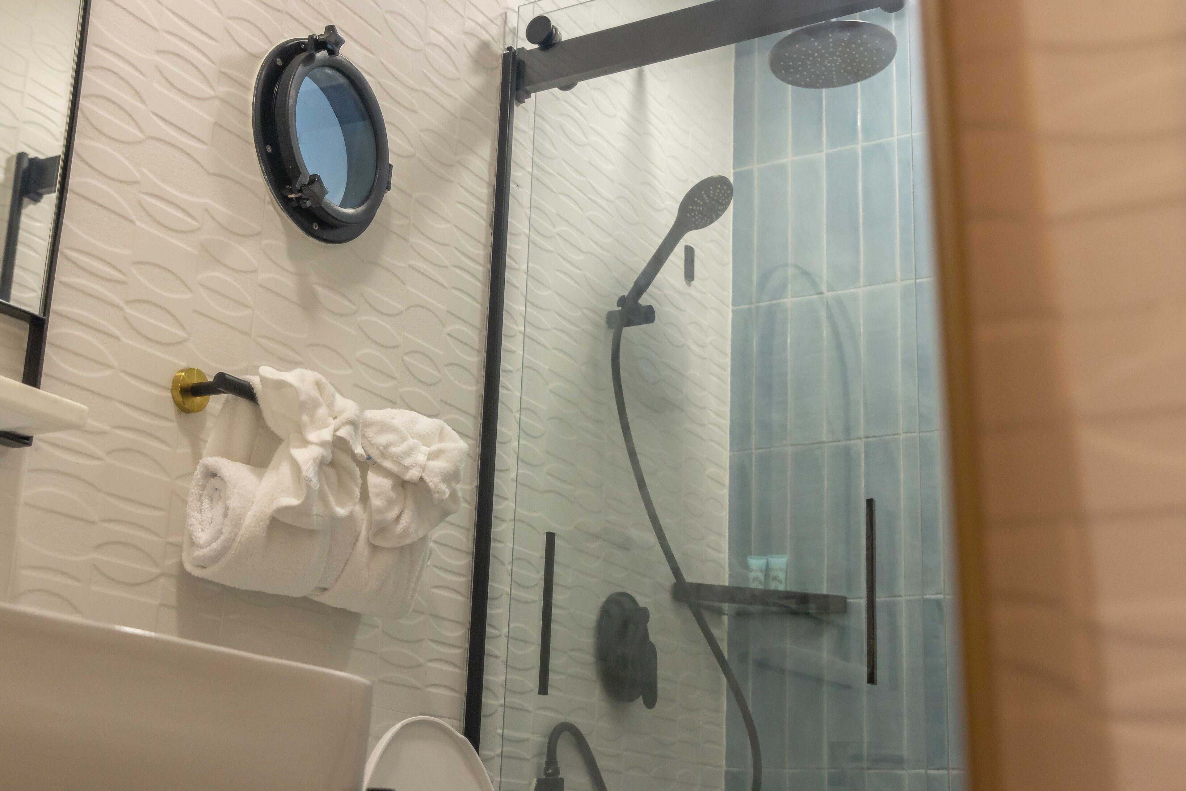 A bathroom with a glass shower enclosure, a handheld showerhead, and a towel rack with a rolled towel.