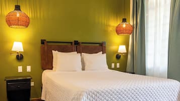 Een hotelkamer met een bed, twee wandlampen, een nachtkastje en een raam met gordijnen.