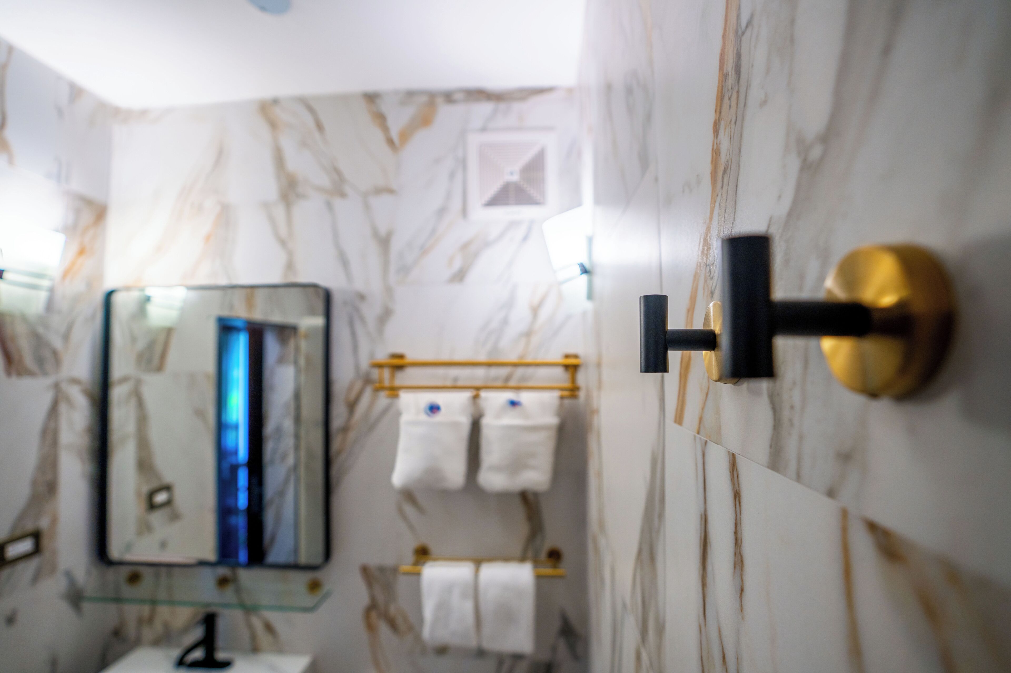 Un bagno con parete in marmo, lavabo con piano in vetro, porta asciugamani e dispenser per asciugamani nero.