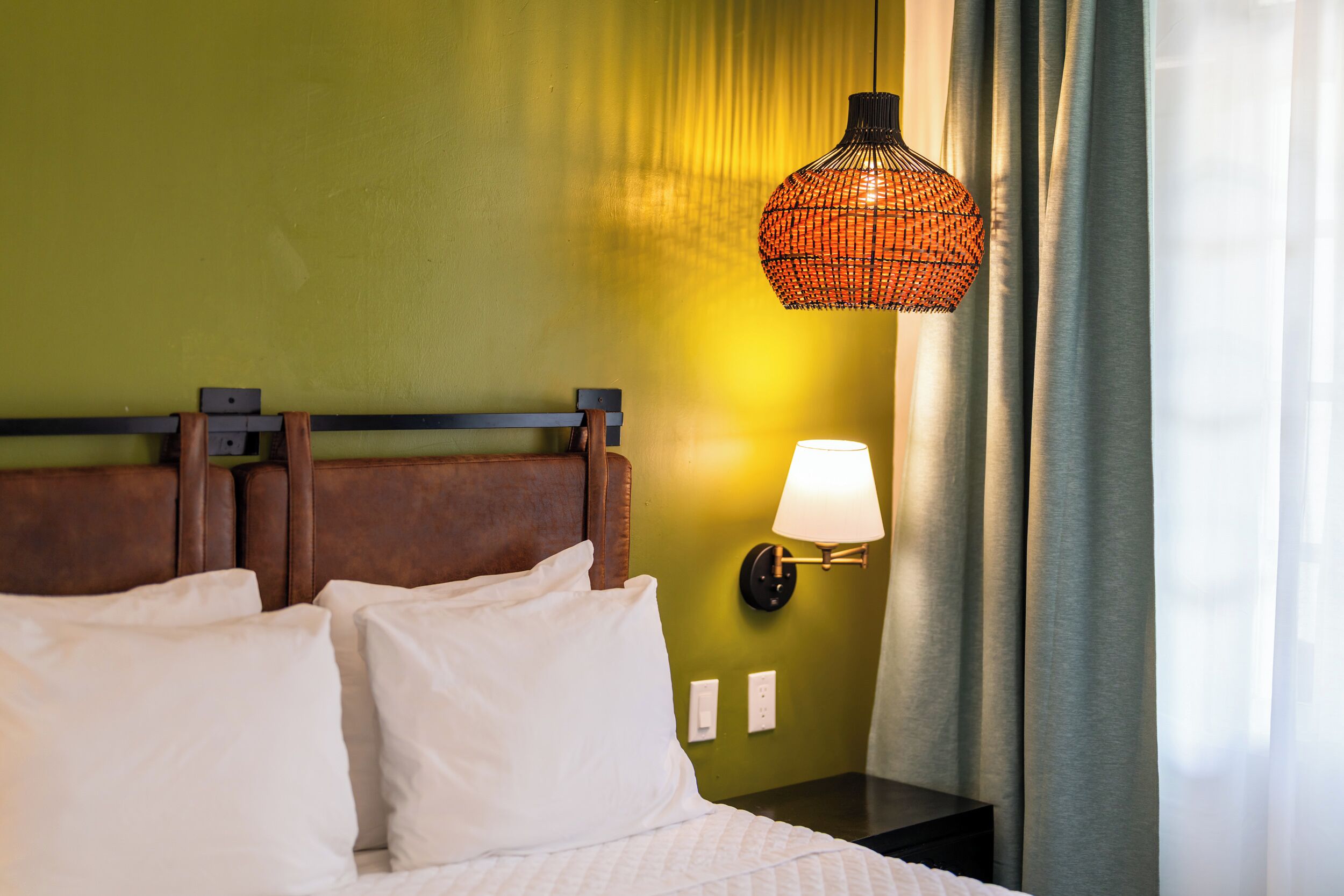 A hotel room with a bed, a nightstand, a lamp, and a wall-mounted light fixture.
