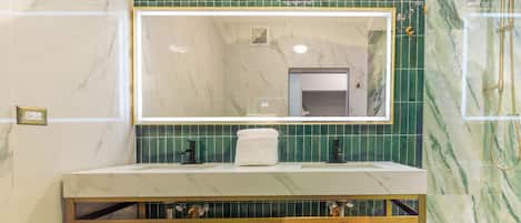 A bathroom with a marble vanity, green tiled walls, and a shower area.