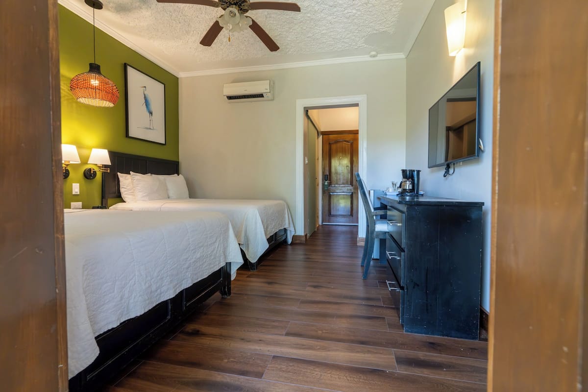 Une chambre d’hôtel avec deux lits, un bureau, une machine à café et un ventilateur de plafond.