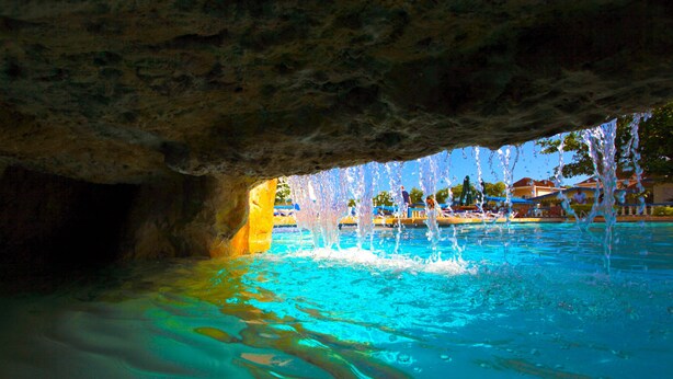 Una piscina con chorros de agua bajo un saliente rocoso.
