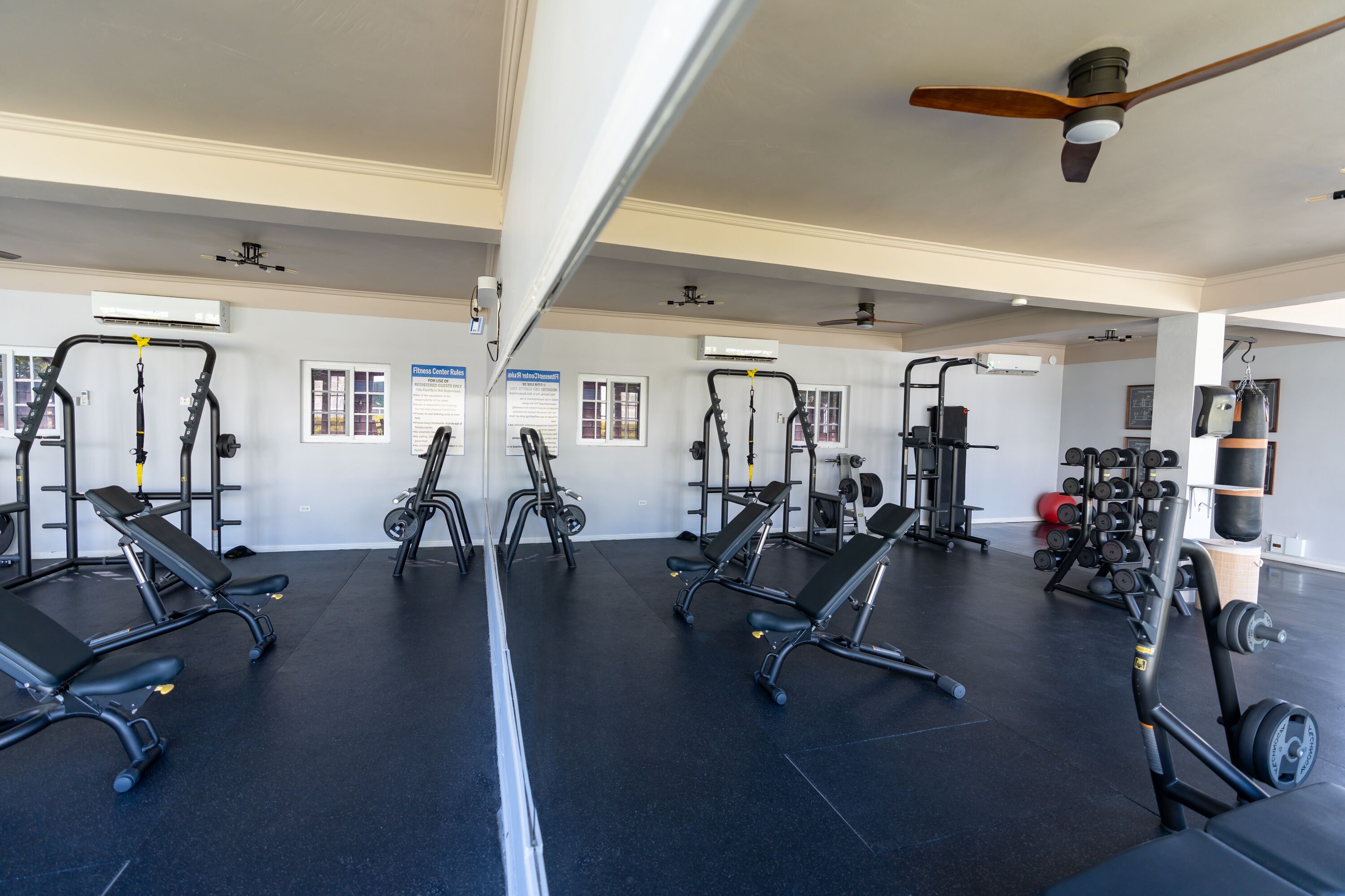 A gym with mirrored walls, ceiling fans, and various exercise equipment.