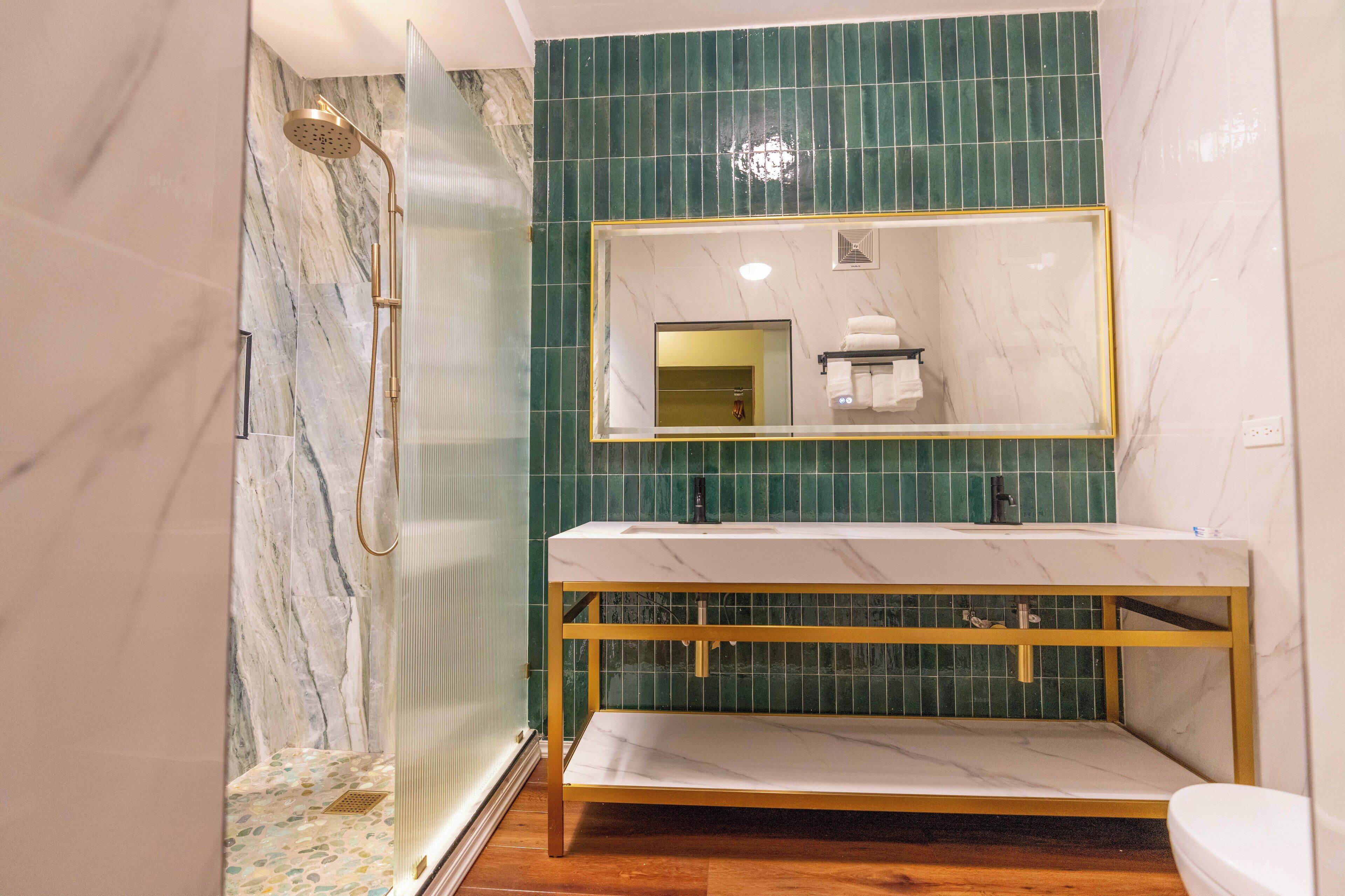 A modern bathroom with a marble vanity, a shower with a gold showerhead, and green tiled walls.
