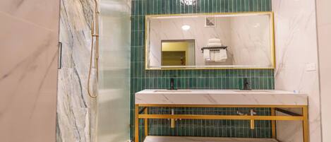 A modern bathroom with a marble vanity, a shower with a gold showerhead, and green tiled walls.