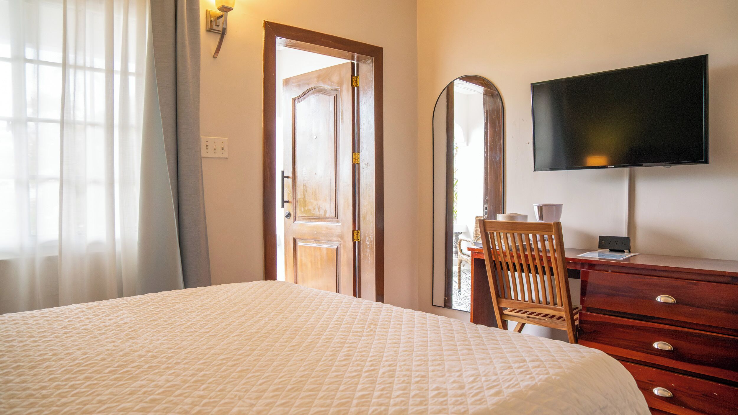 A hotel room with a bed, a wooden dresser, a television, and a mirror.