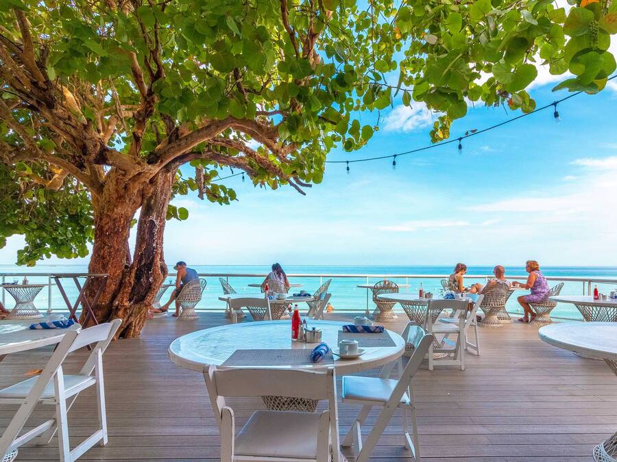 A deck with round tables and chairs, overlooking a beach with a clear view of the ocean.
