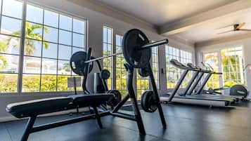 Un gimnasio con equipo de ejercicio, ventanas amplias y un ventilador de techo.