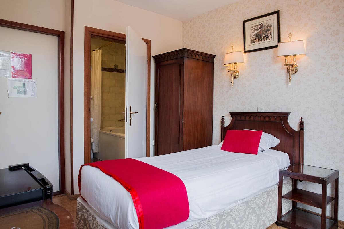 Habitación de hotel con cama, armario de madera, mesita de vidrio y zona de ducha.