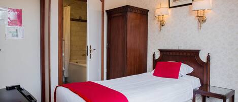 A hotel room with a bed, a wooden wardrobe, a glass side table, and a shower area.