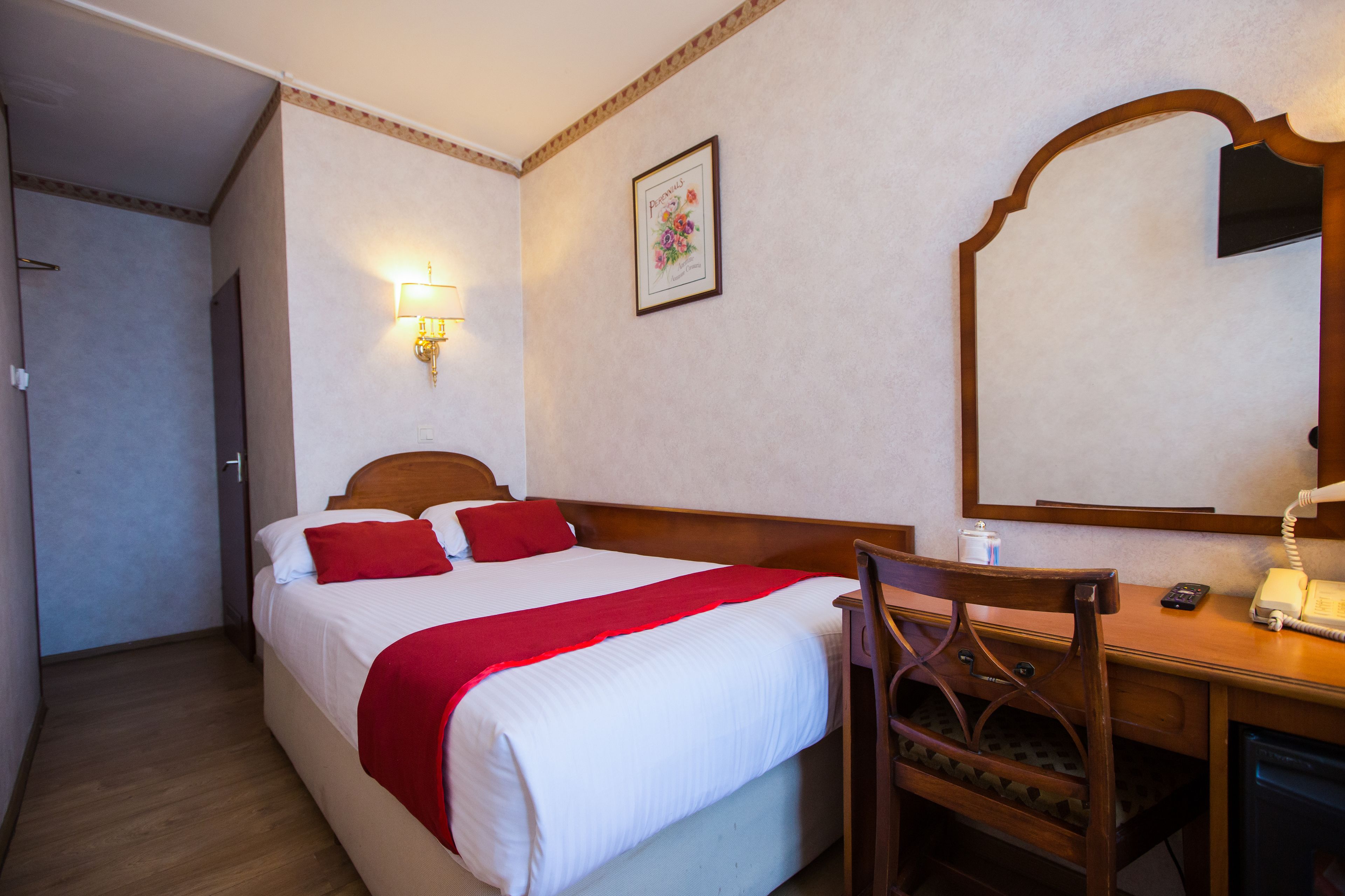 A hotel room with a bed, a desk with a telephone, and a mirror.
