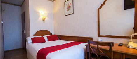 A hotel room with a bed, a desk with a telephone, and a mirror.