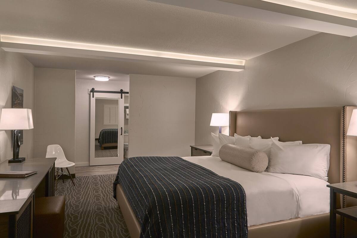 A hotel room with a bed, bedside tables, a desk, a chair, and a bathroom door.