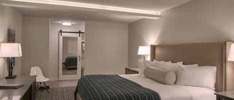 A hotel room with a bed, bedside tables, a desk, a chair, and a bathroom door.