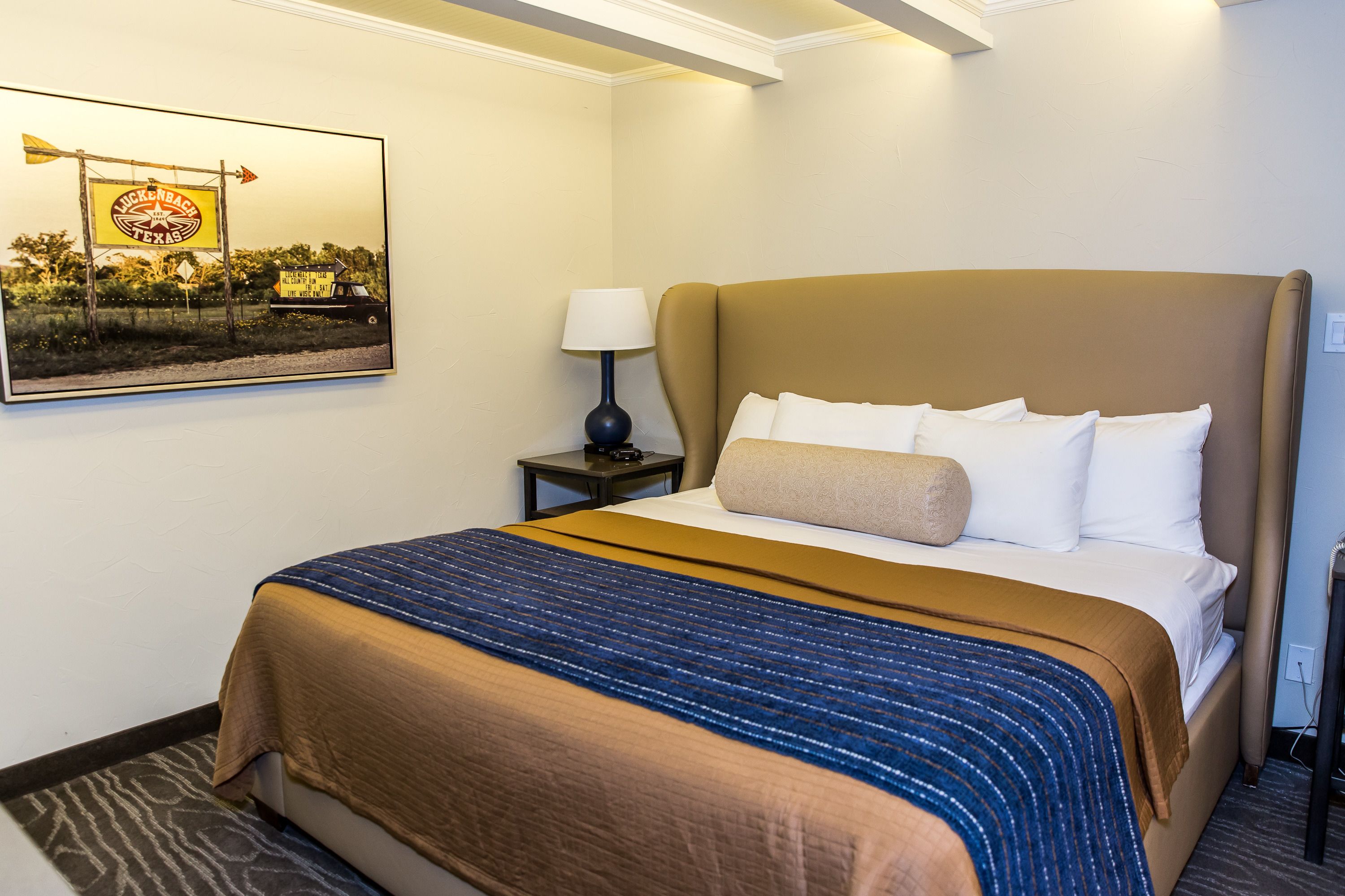 A hotel room with a large bed, a nightstand, a lamp, and a framed picture on the wall.