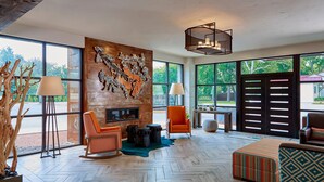 Amplia habitación con grandes ventanales, una obra de arte de madera en la pared y muebles modernos, incluyendo un sofá, sillas y una mesa.