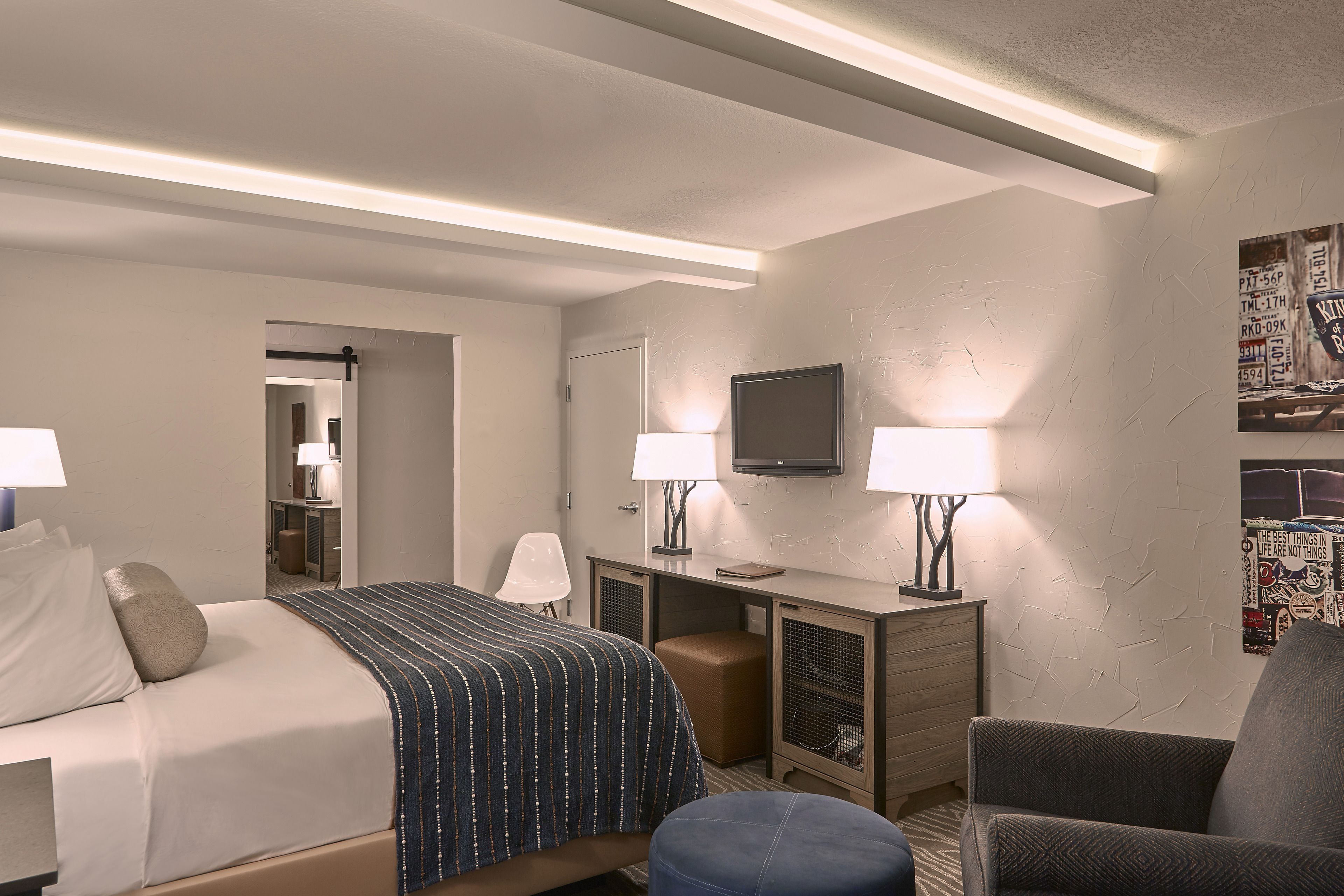 Une chambre d’hôtel avec un lit, deux tables de chevet avec des lampes, un bureau, une chaise et un téléviseur fixé au mur.