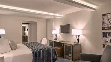 Ein Hotelzimmer mit einem Bett, zwei Nachttischen mit Lampen, einem Schreibtisch, einem Sessel und einem Fernseher an der Wand.