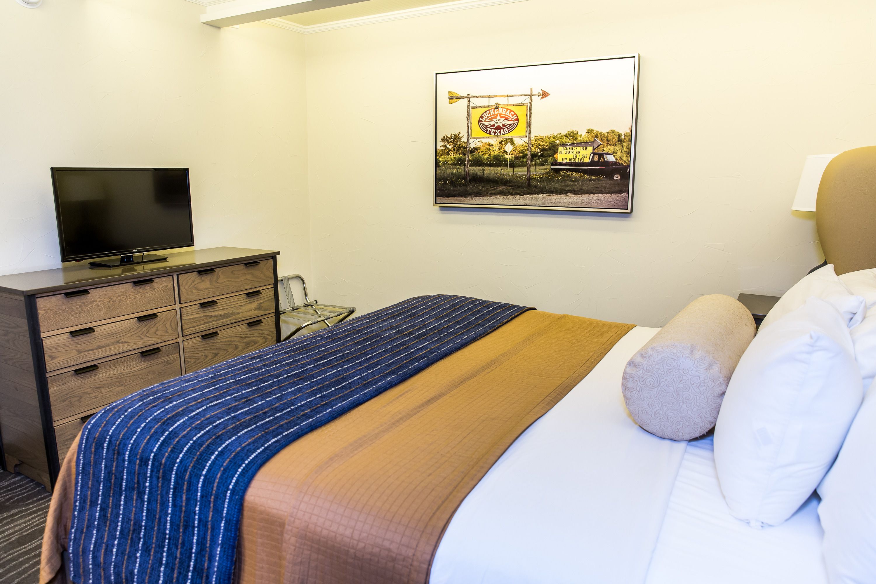 A hotel room with a bed, a television on a dresser, and a framed picture on the wall.