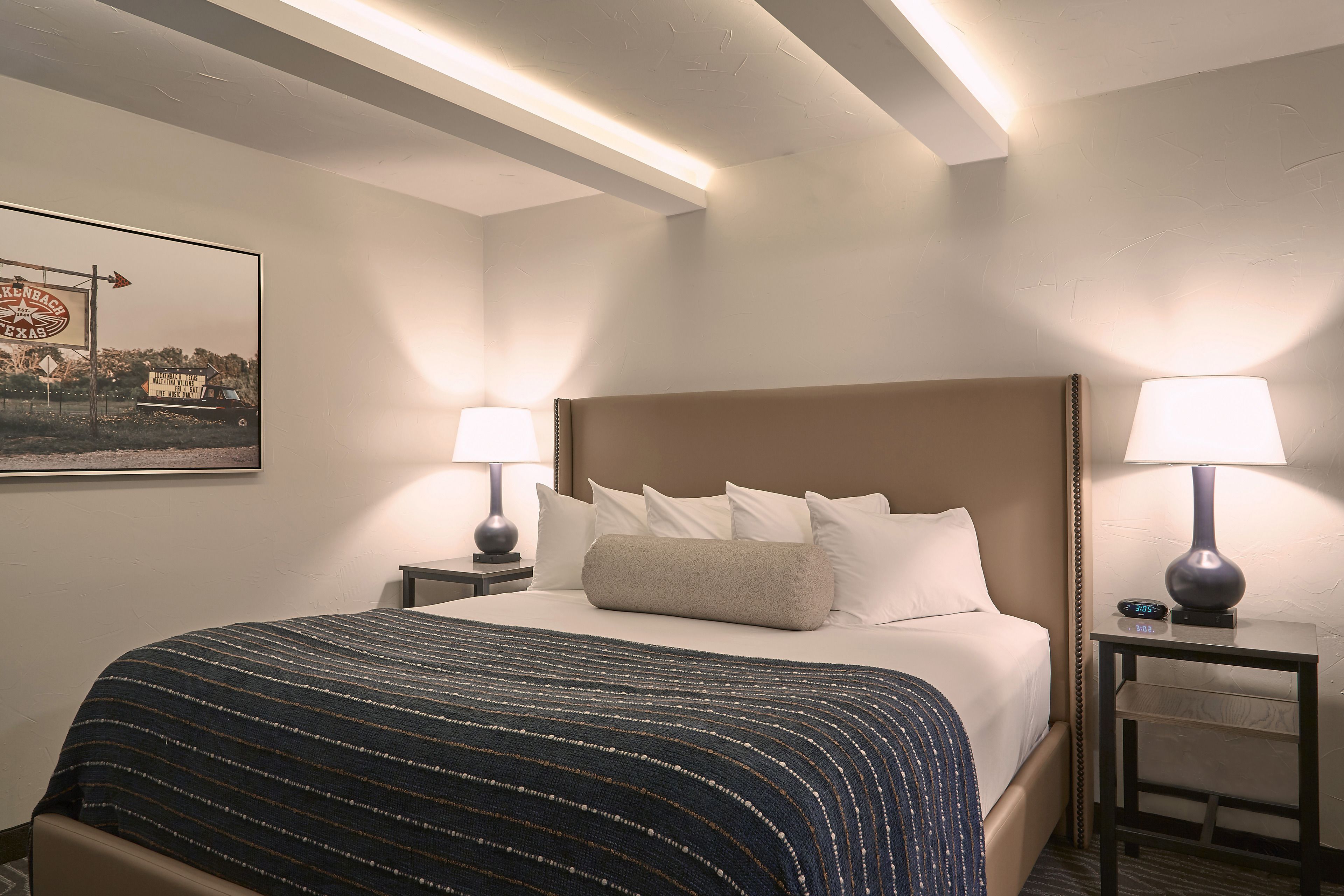 A hotel room with a large bed, two bedside tables with lamps, a framed picture on the wall, and a ceiling with exposed beams.