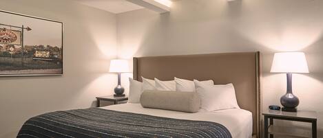 A hotel room with a large bed, two bedside tables with lamps, a framed picture on the wall, and a ceiling with exposed beams.
