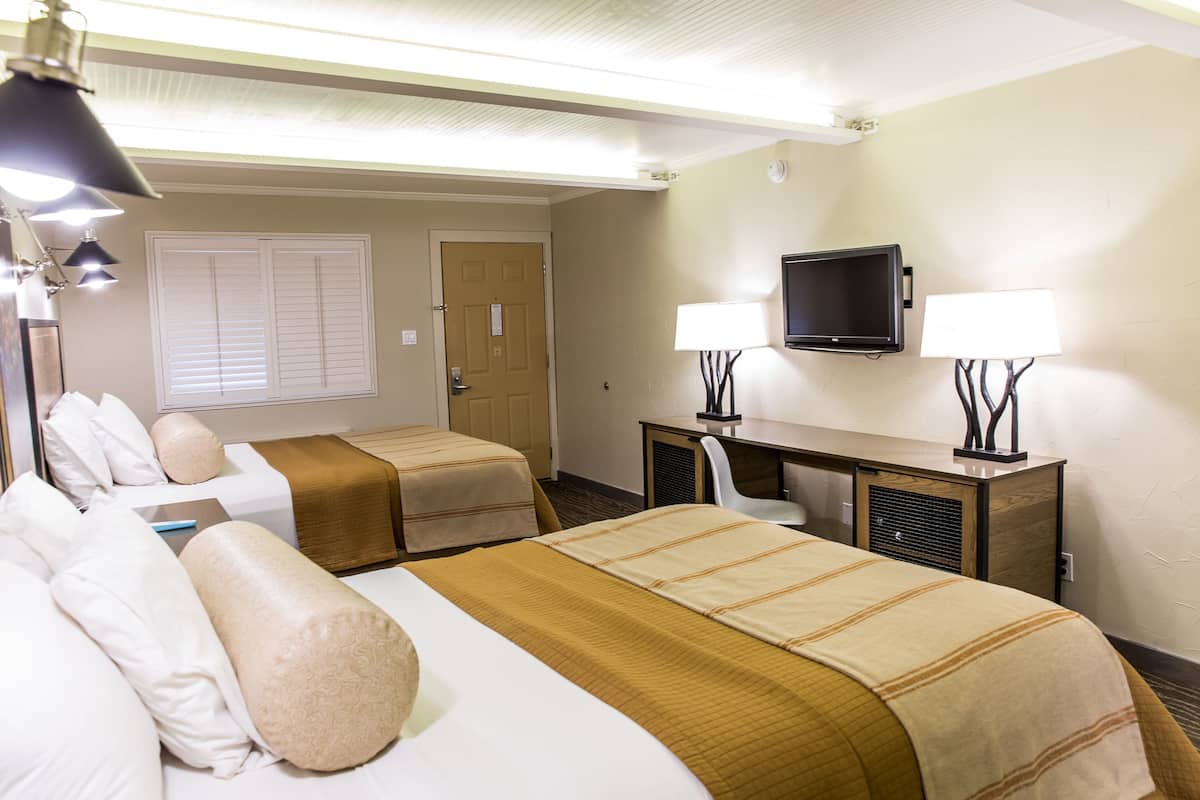 A hotel room with two beds, a desk, a TV, and two lamps.