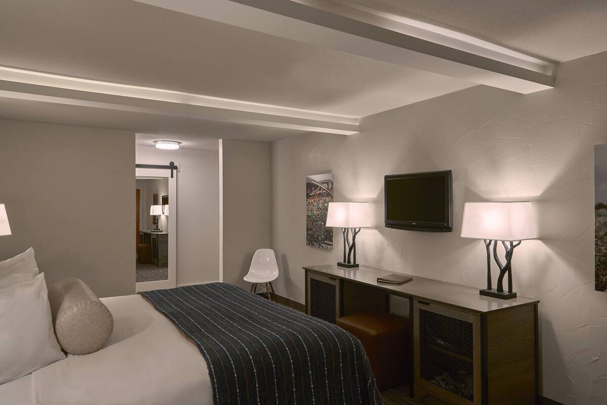 A hotel room with a bed, bedside lamps, a desk, a television, and a mirror.
