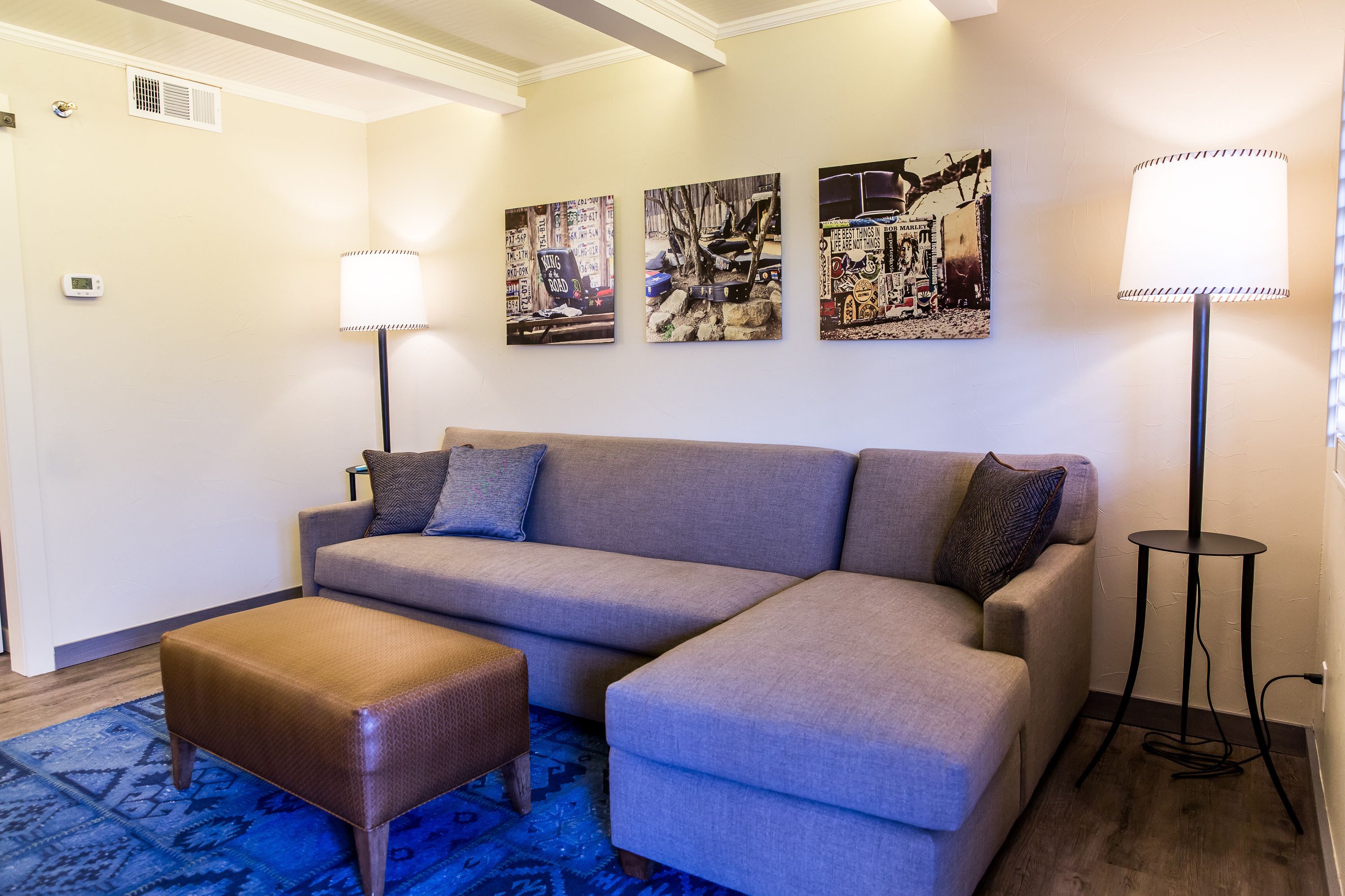 A modern living room with a grey sectional sofa, a brown ottoman, and three wall-mounted artworks.
