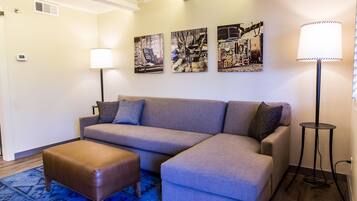 A modern living room with a grey sectional sofa, a brown ottoman, and three wall-mounted artworks.