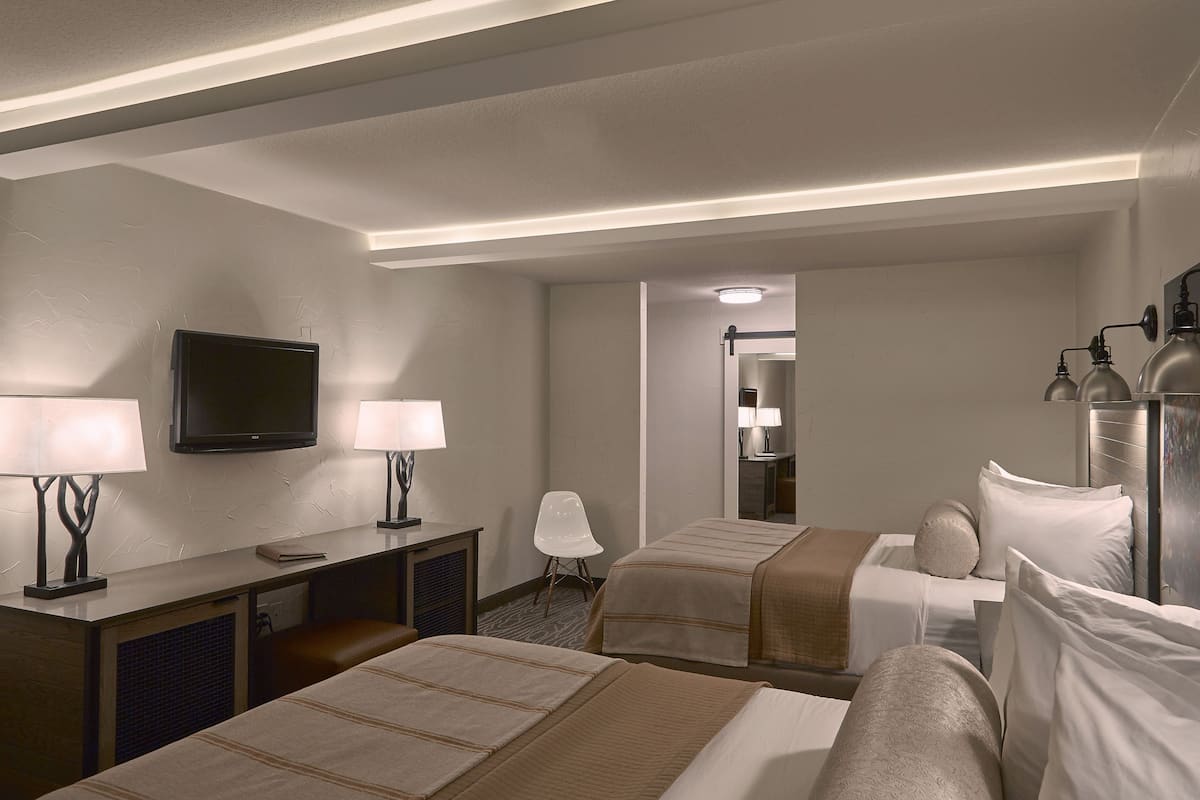 A hotel room with two beds, a desk with a TV, and a chair.